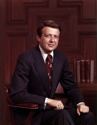 James Eubert Holshouser, Jr. sitting in front of a wood paneled wall and books.